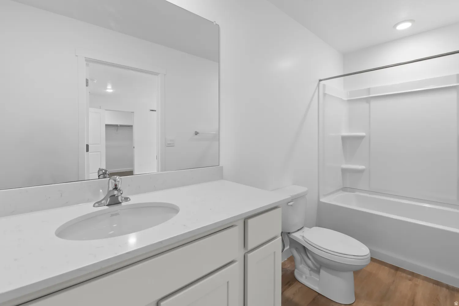 Bathroom featuring a white vanity with an undermount sink, a large wall-mounted mirror, a white toilet, and a white tub/shower combination with integrated shelving