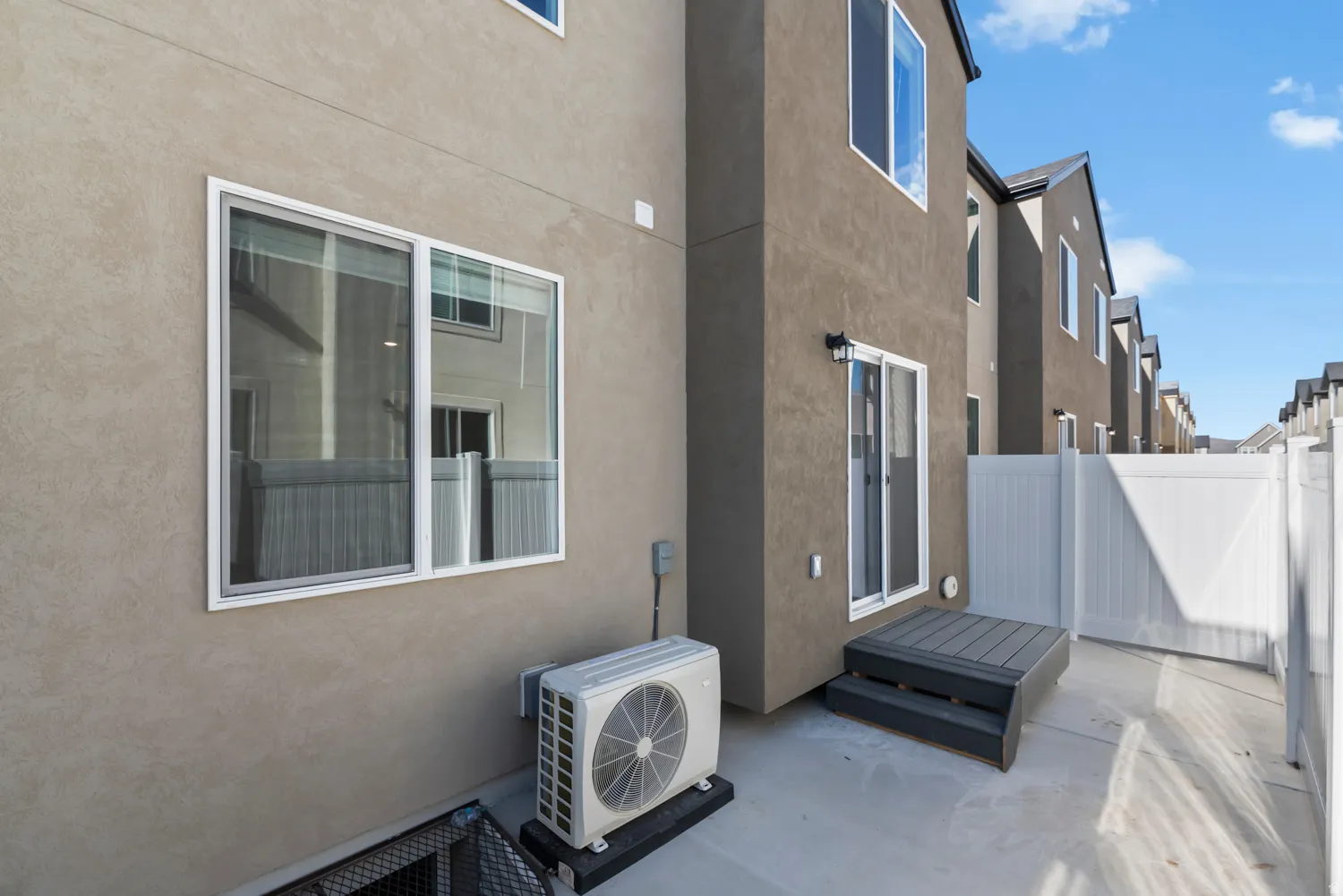 Exterior stucco walls with multiple windows, a sliding glass door, and a white vinyl privacy fence