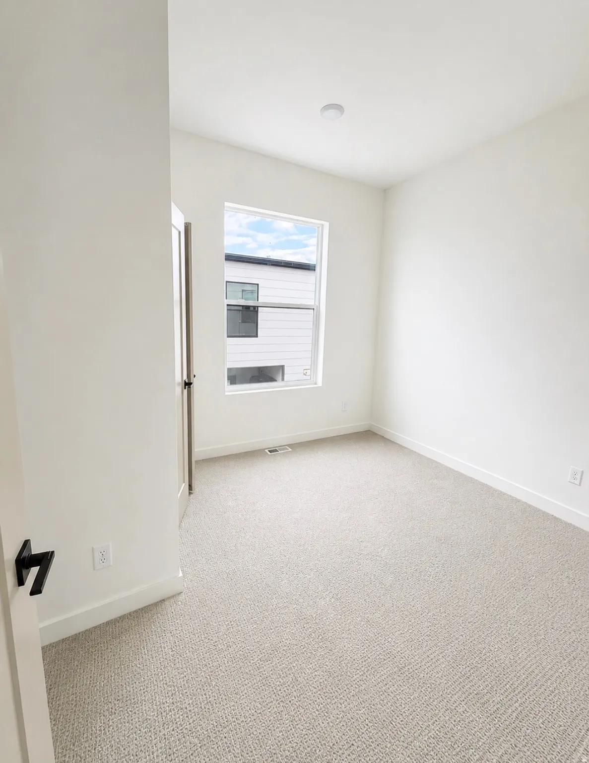 Bright interior space featuring light-toned carpet, a window with exterior views, white walls, and a recessed ceiling light
