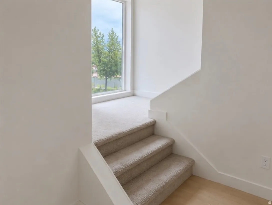 Carpeted staircase with light-toned walls and a window at the landing