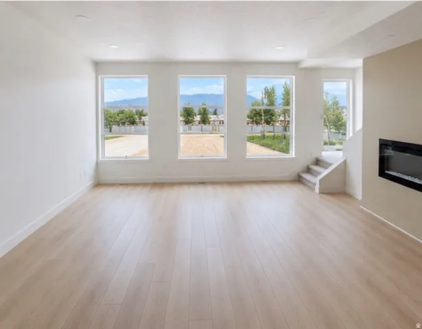 Expansive living area with light wood-finish flooring, recessed lighting, and a linear electric fireplace