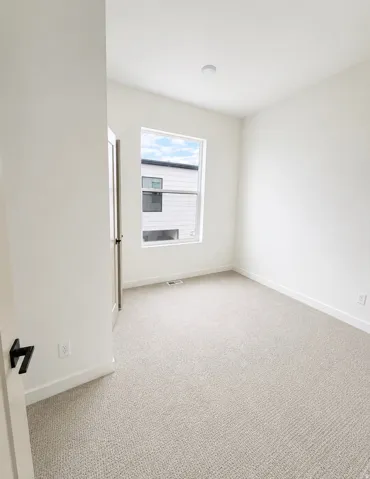 Bright interior space featuring light-toned carpet, a window with exterior views, white walls, and a recessed ceiling light