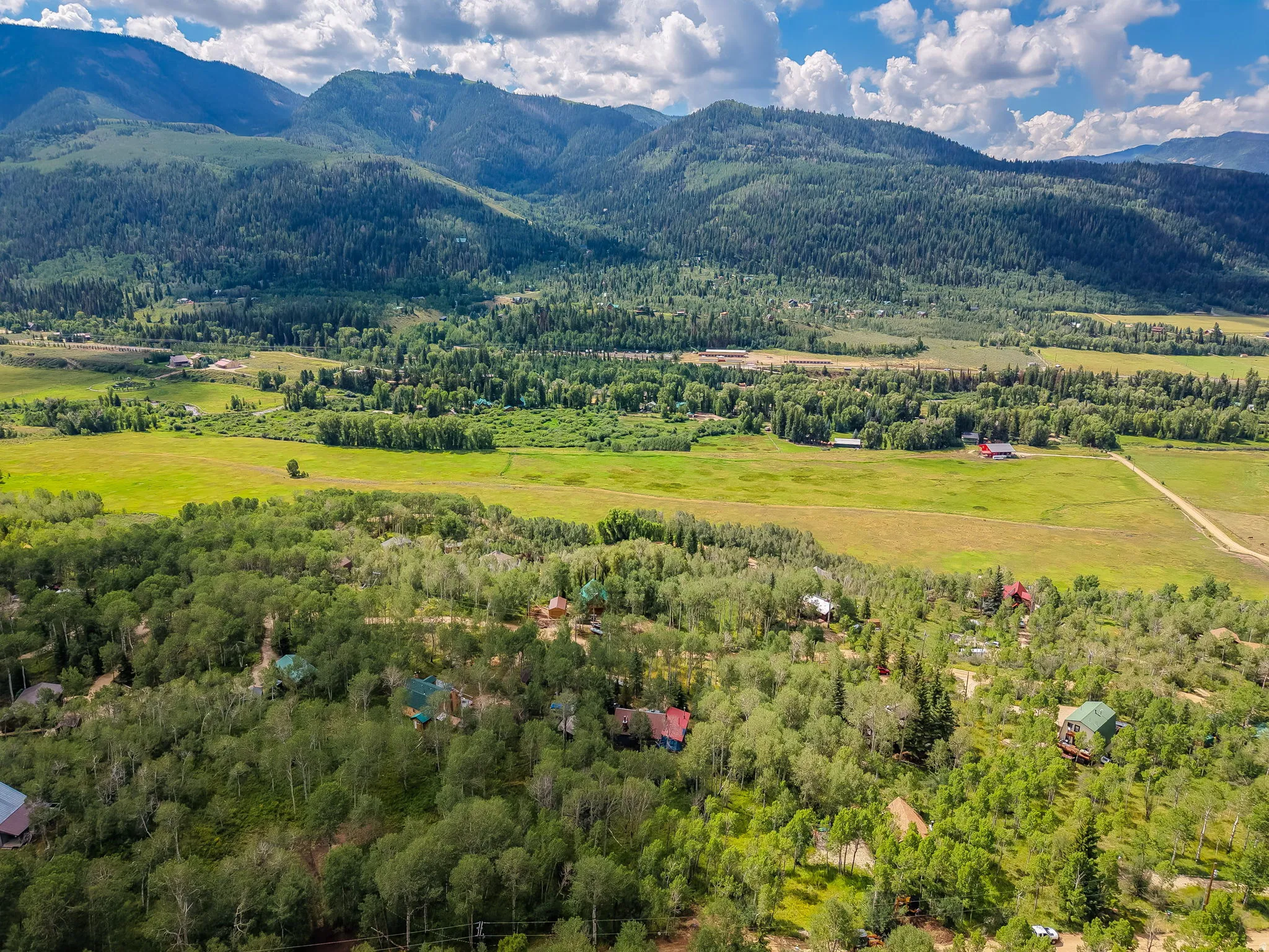 Expansive mountain landscape featuring a broad valley with lush green fields and dense forests
