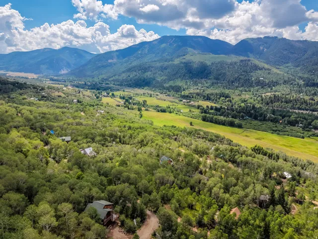 Expansive valley with verdant fields and dense tree coverage, bordered by distant mountains under a blue sky with white clouds