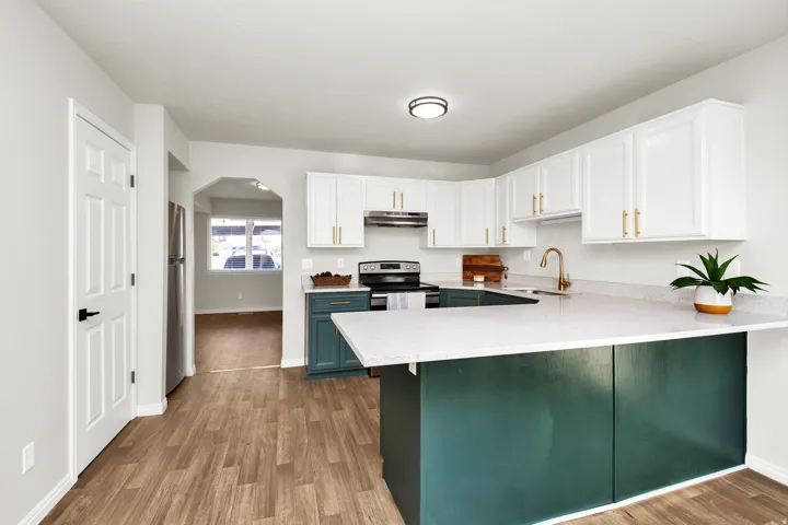Modern kitchen featuring wood-finish flooring, white upper cabinetry, and contrasting deep teal lower cabinetry with gold-tone hardware