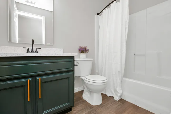 Bathroom featuring a dark green vanity with gold-tone hardware, a white speckled countertop, a matte black faucet, and wood-finish flooring