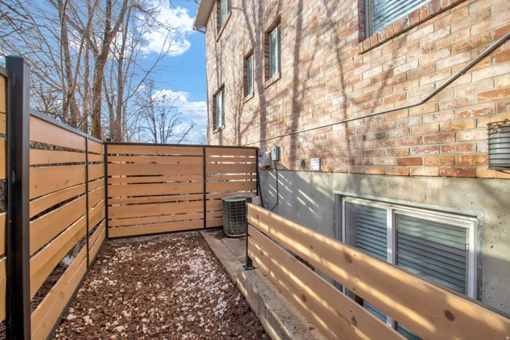 Enclosed outdoor space featuring a slatted wood fence with dark posts, a mixed gravel and wood chip ground covering, and a brick exterior wall