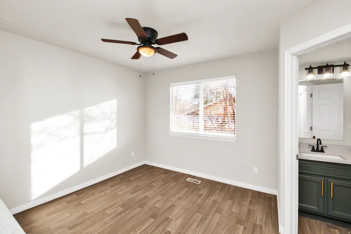 Bright room featuring wood-finish flooring, a ceiling fan with integrated lighting, and a window with blinds