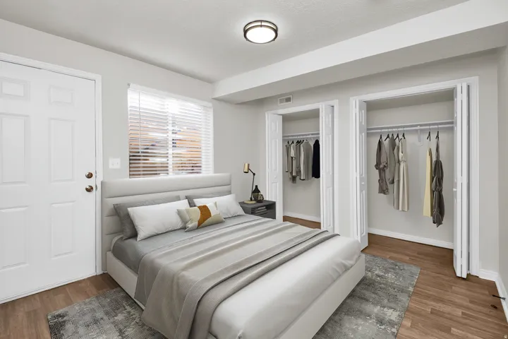 Bedroom featuring wood-finish flooring, two bi-fold closet doors, a ceiling-mounted flush light fixture, a window with blinds, and a white panel door