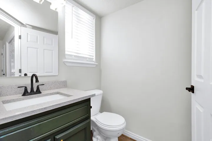 Powder room featuring a dark green vanity with a light speckled countertop, an undermount sink, and a matte black faucet