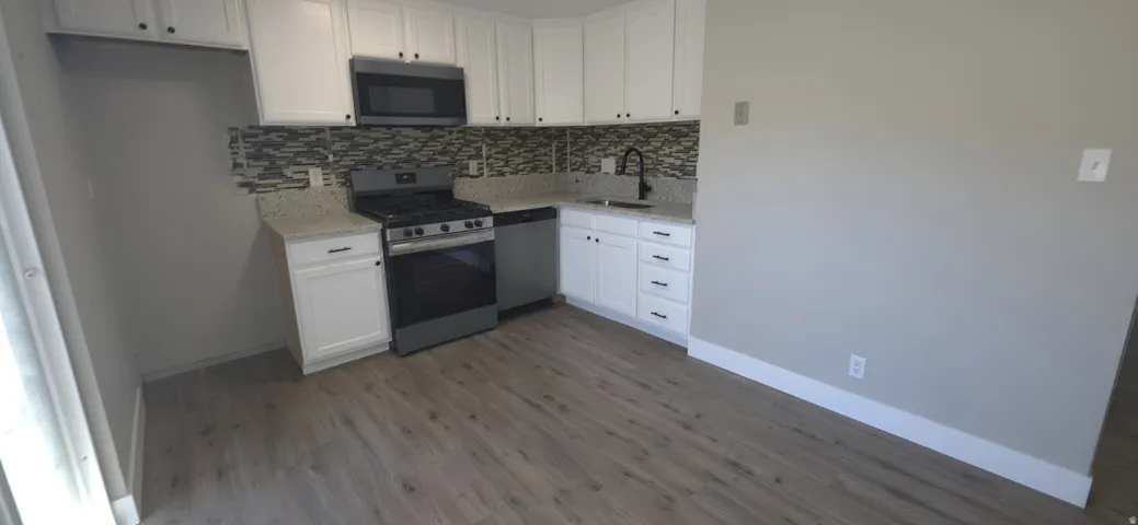 Kitchen featuring white cabinetry, light-toned countertops, tile backsplash, stainless steel appliances, and wood-finish flooring