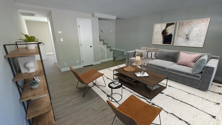 Open-concept living area featuring light wood-finish flooring, neutral wall tones, a built-in staircase, and a white interior door