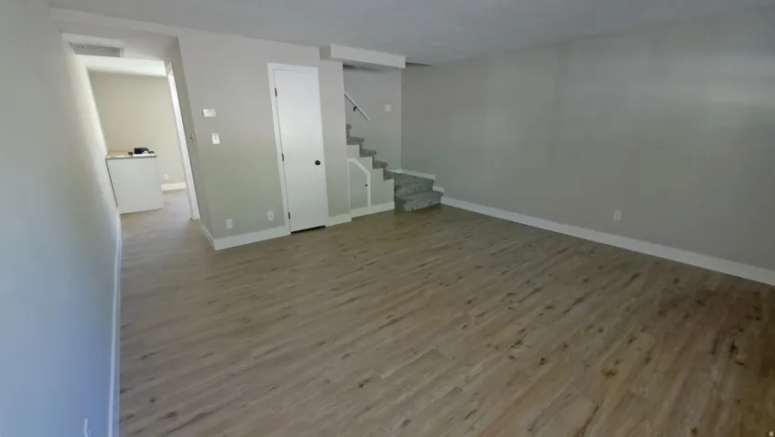 Open-concept living area featuring wood-finish flooring, light gray wall tones, white baseboards, and a staircase with patterned carpeting