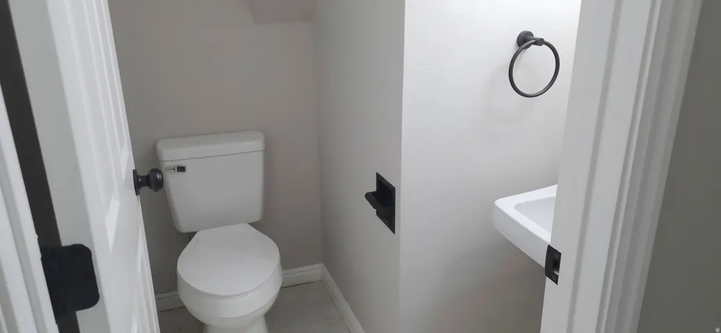 Powder room featuring a wall-mounted sink, a toilet, a matte black towel ring, a recessed toilet paper holder, and light-toned wall paint