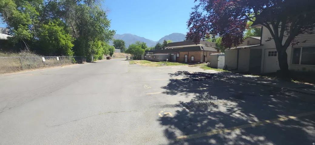 Paved parking area with painted space markers, bordered by mature trees and a chain-link fence