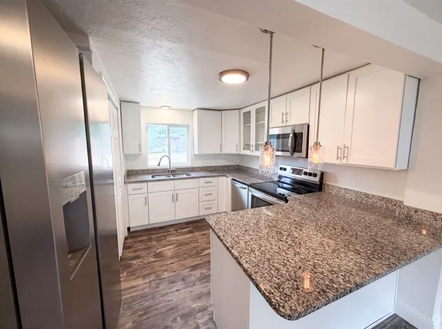 Modern kitchen featuring white cabinetry, stainless steel appliances, granite countertops, wood-finish flooring, and pendant lighting