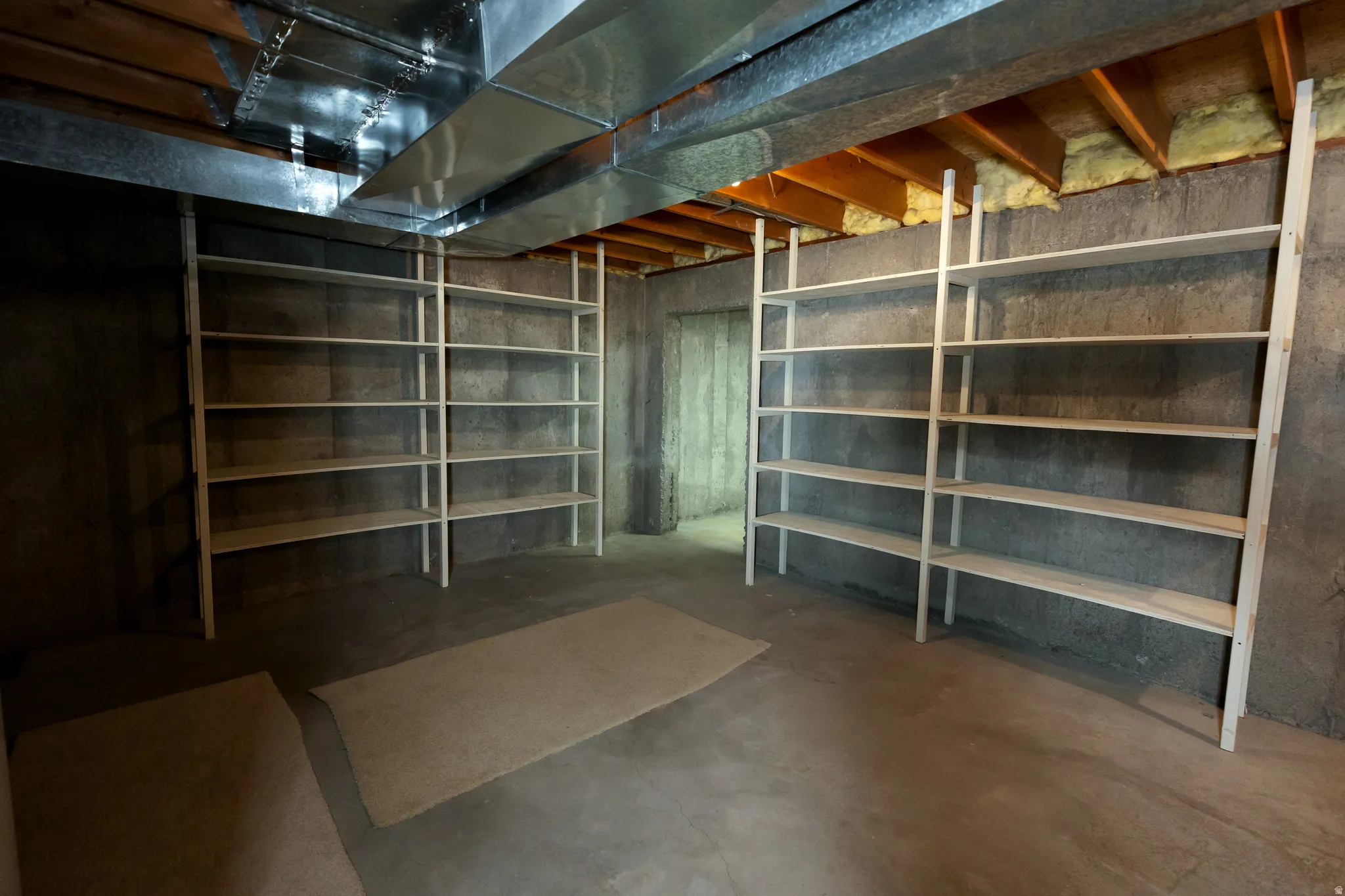 Unfinished basement featuring concrete flooring, exposed joists, and extensive built-in shelving units