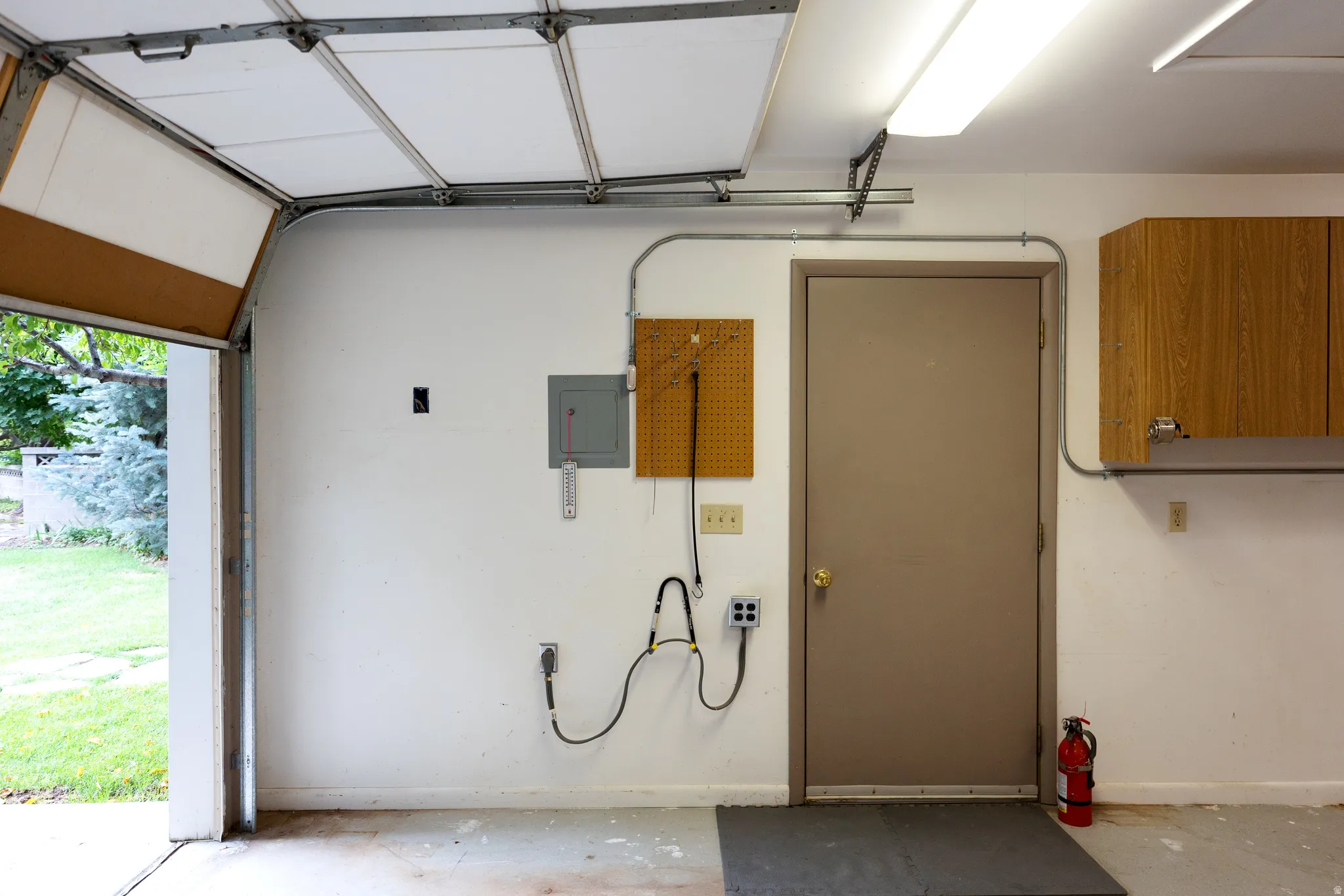 Attached garage interior featuring a roll-up door, fluorescent overhead lighting, wall-mounted electrical panel, and wood-finish cabinetry