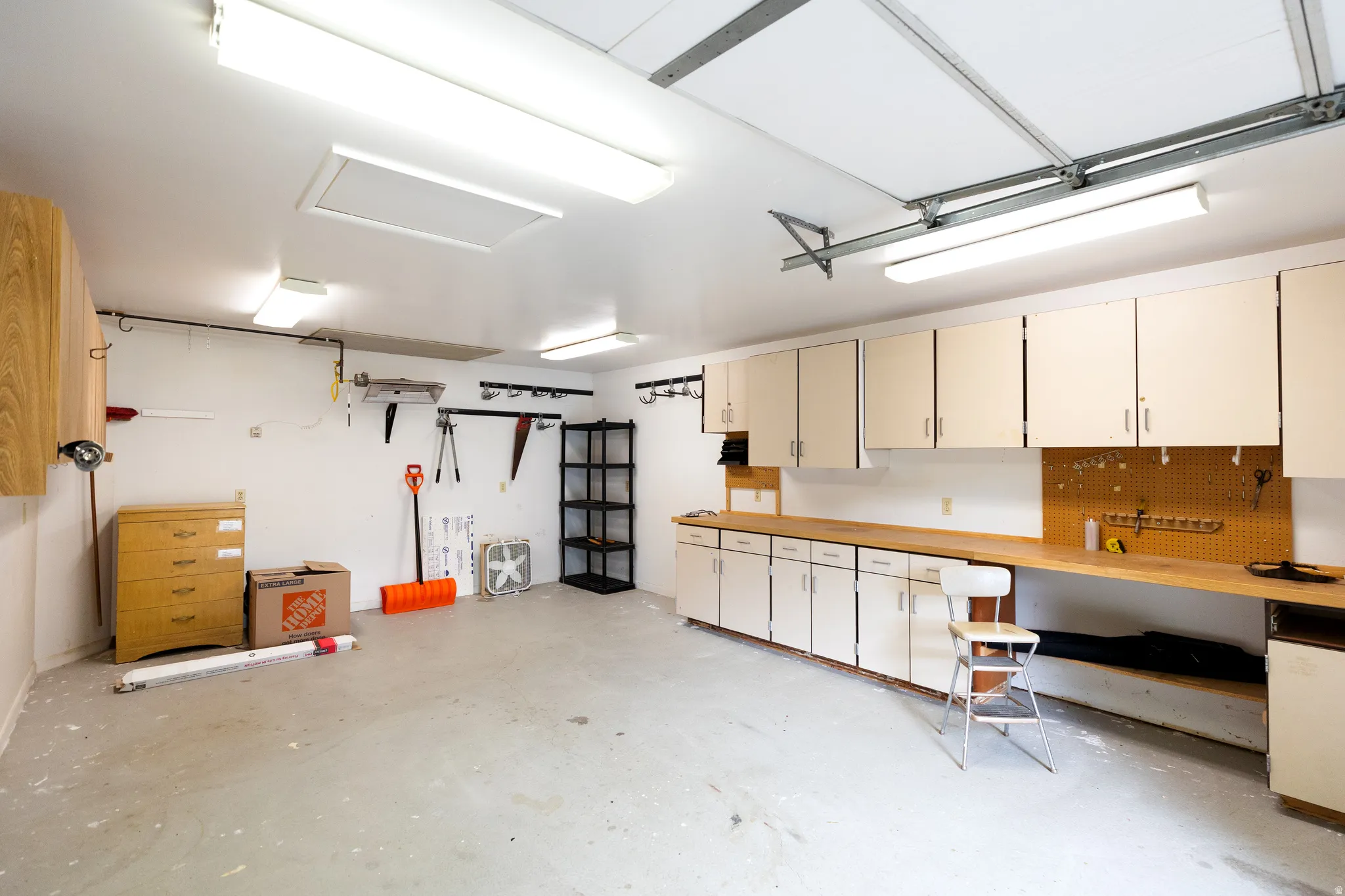 Spacious garage featuring extensive built-in cabinetry, long wood-finish countertops, and a large pegboard for organization