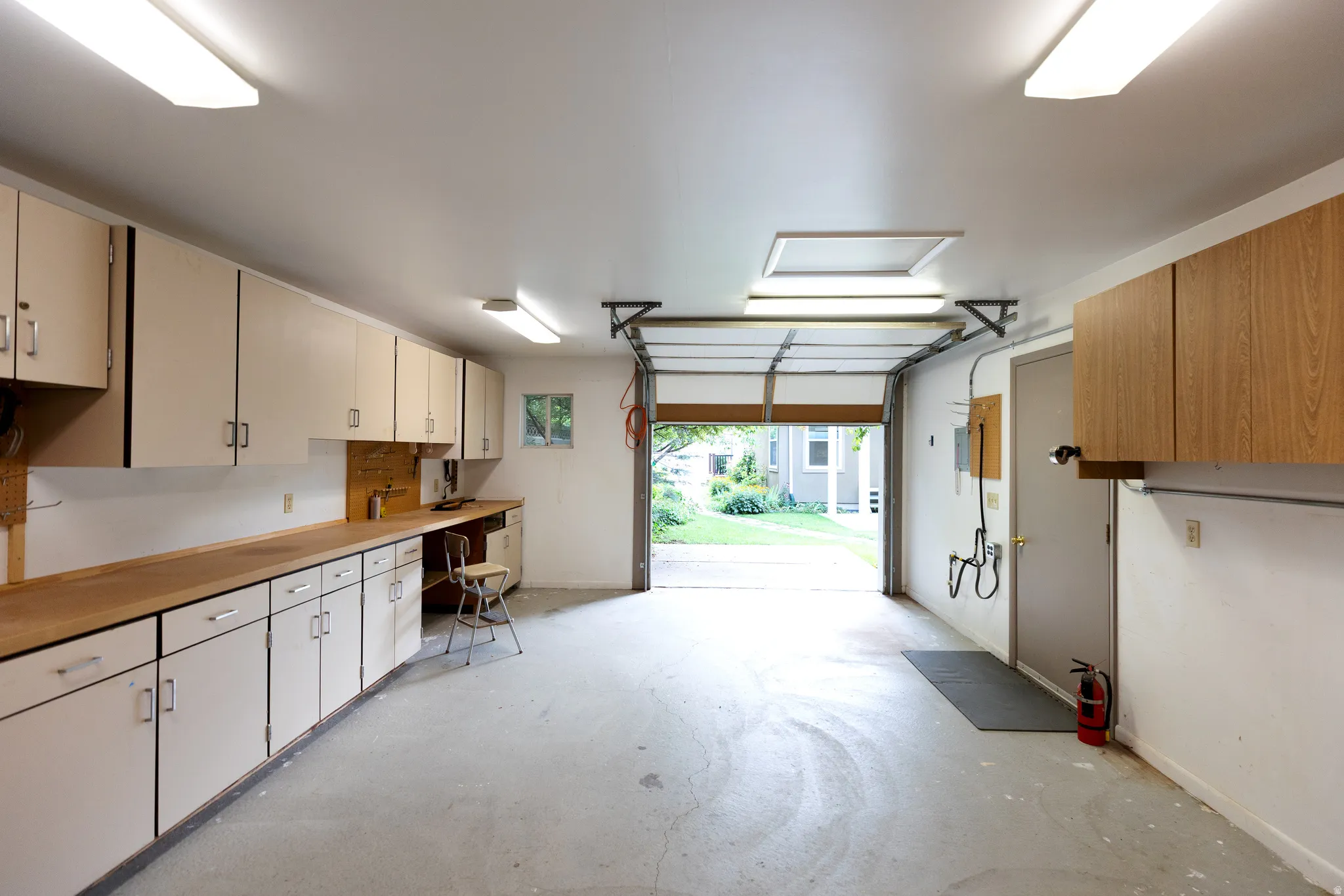 Spacious garage featuring extensive built-in cabinetry, a wood-finish countertop workspace, and overhead fluorescent lighting