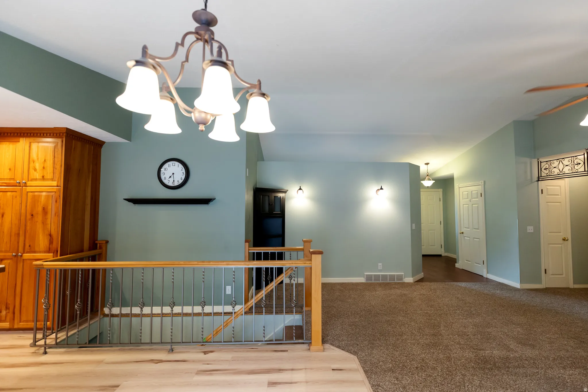 Open-concept area featuring wood-finish flooring, a metal and wood baluster railing, and a decorative chandelier