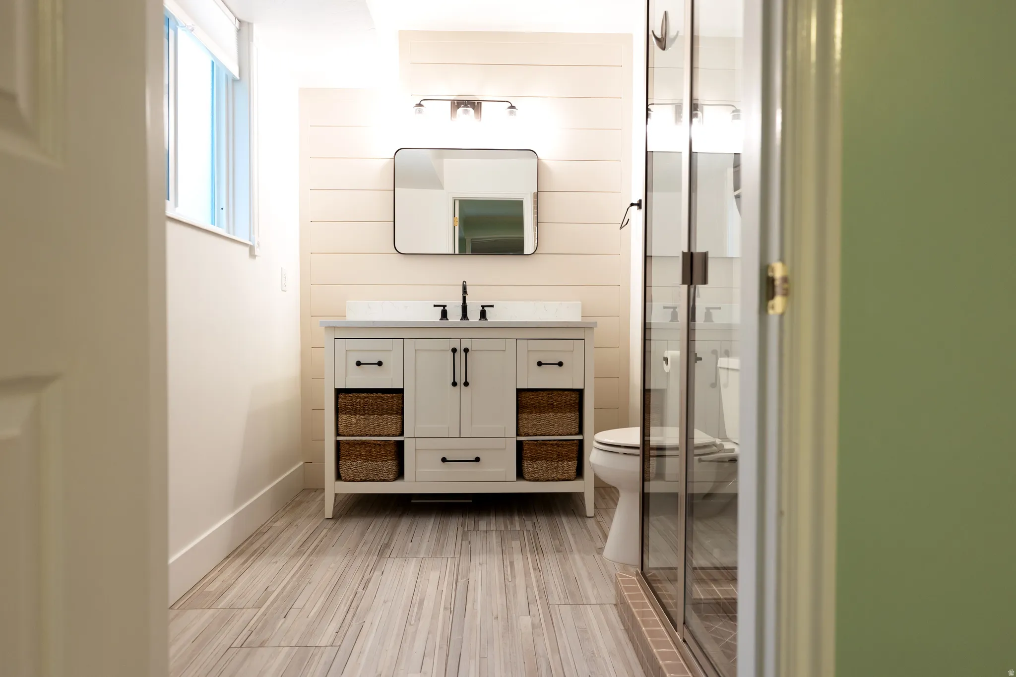 Modern bathroom featuring a white vanity with black hardware, plank-style wall paneling, and wood-finish tile flooring