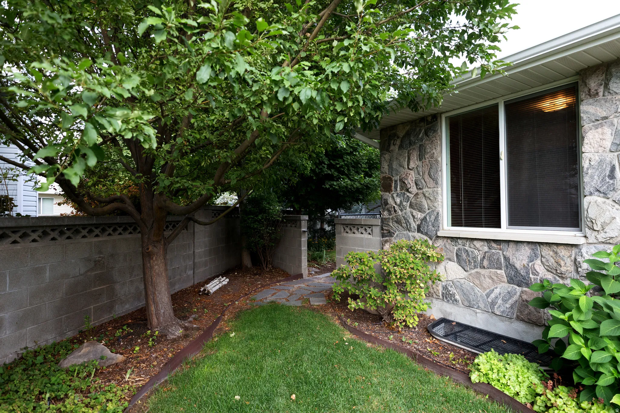 Stone veneer exterior with a large window, complemented by a mature tree and a block wall with decorative elements