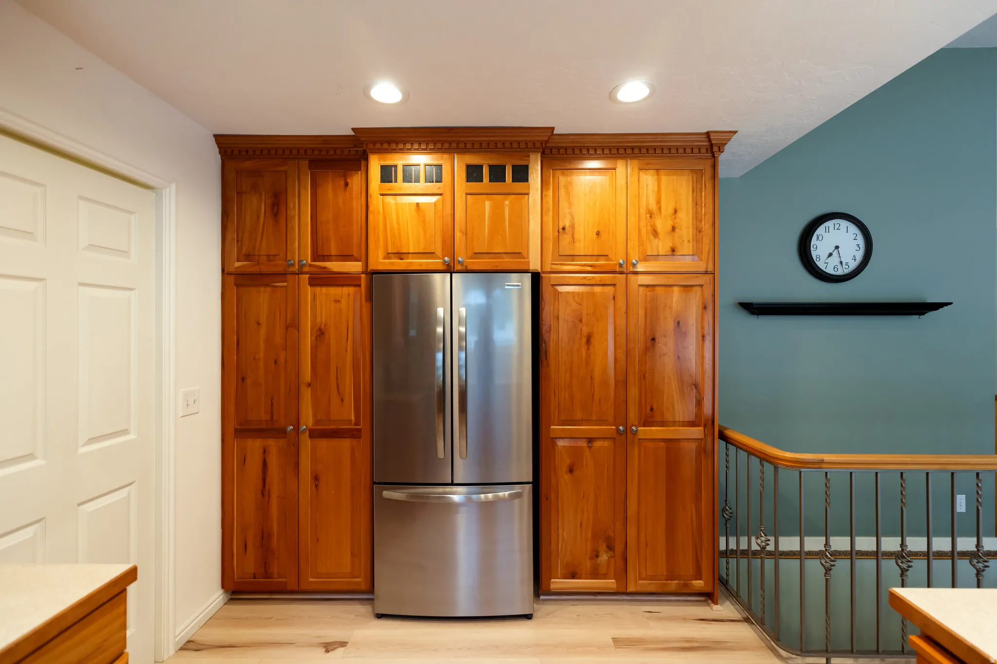 Custom wood-finish cabinetry with crown molding and integrated lighting, surrounding a stainless steel refrigerator