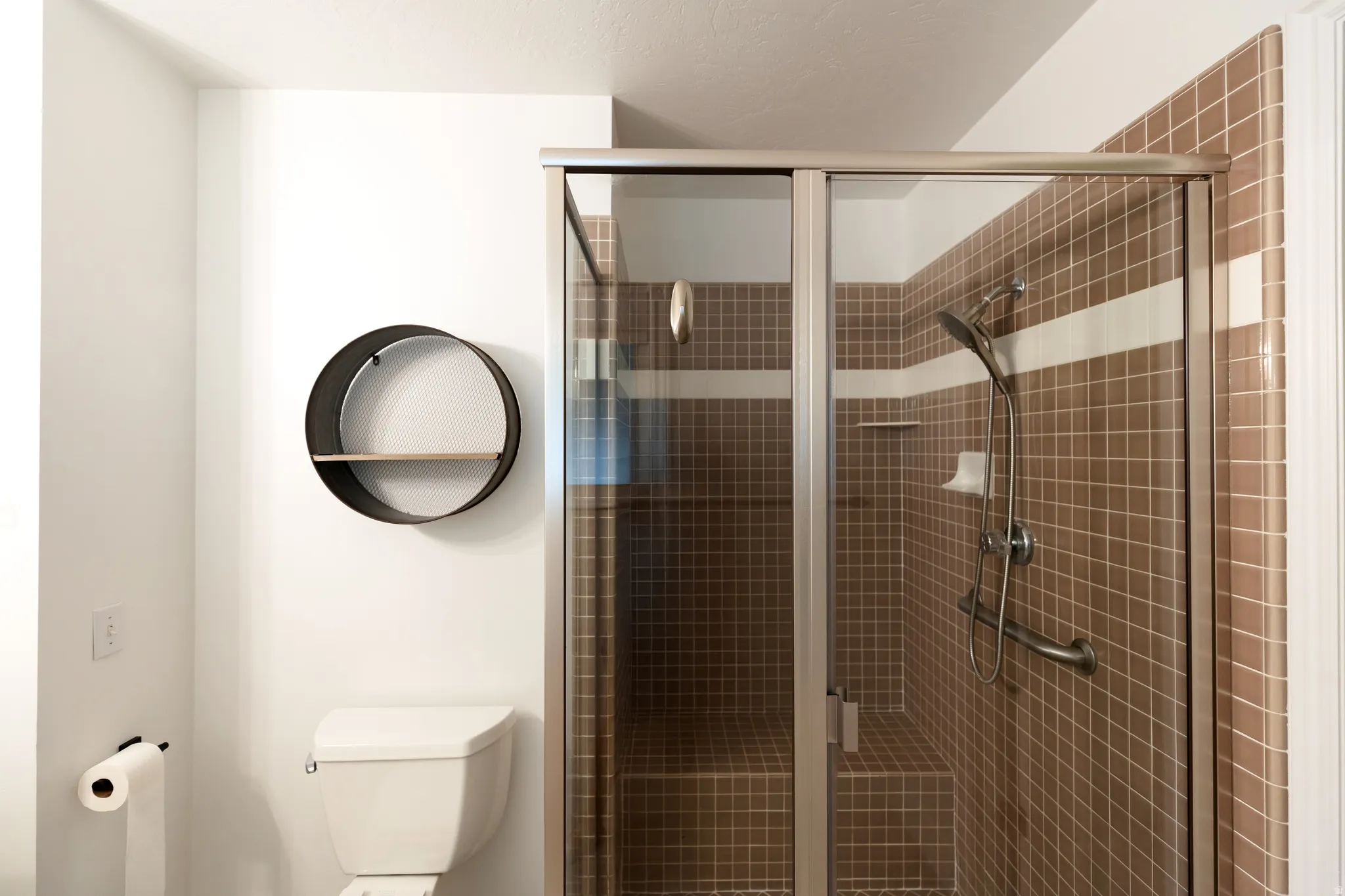Shower enclosure featuring brown square tiles with a white accent band, a built-in shower bench, and a handheld showerhead
