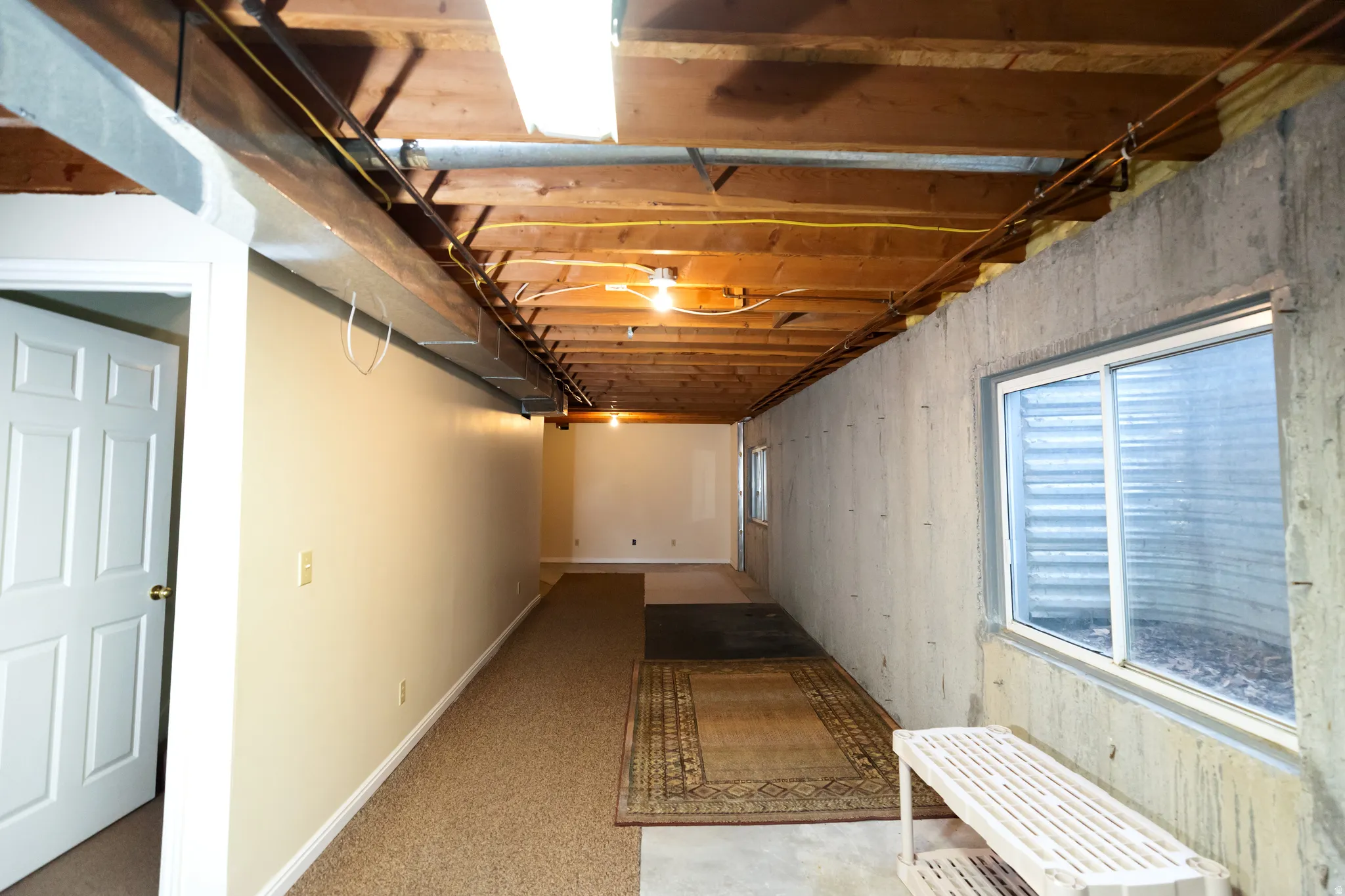 Unfinished basement featuring exposed wood joists and concrete walls, with two sliding windows providing natural light