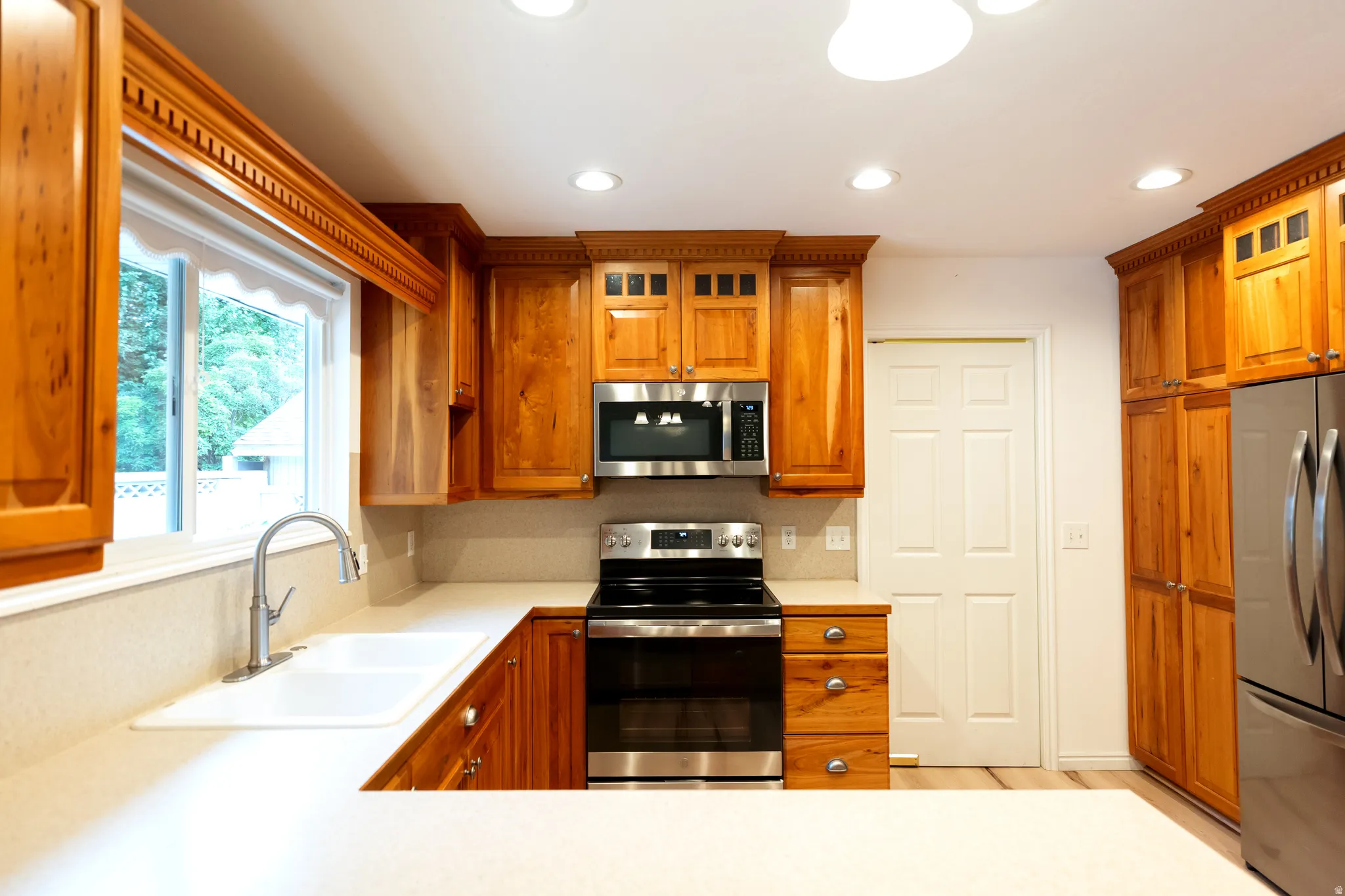 Kitchen featuring wood cabinetry with crown molding, light-toned countertops, and stainless steel appliances including a range, microwave, and refrigerator