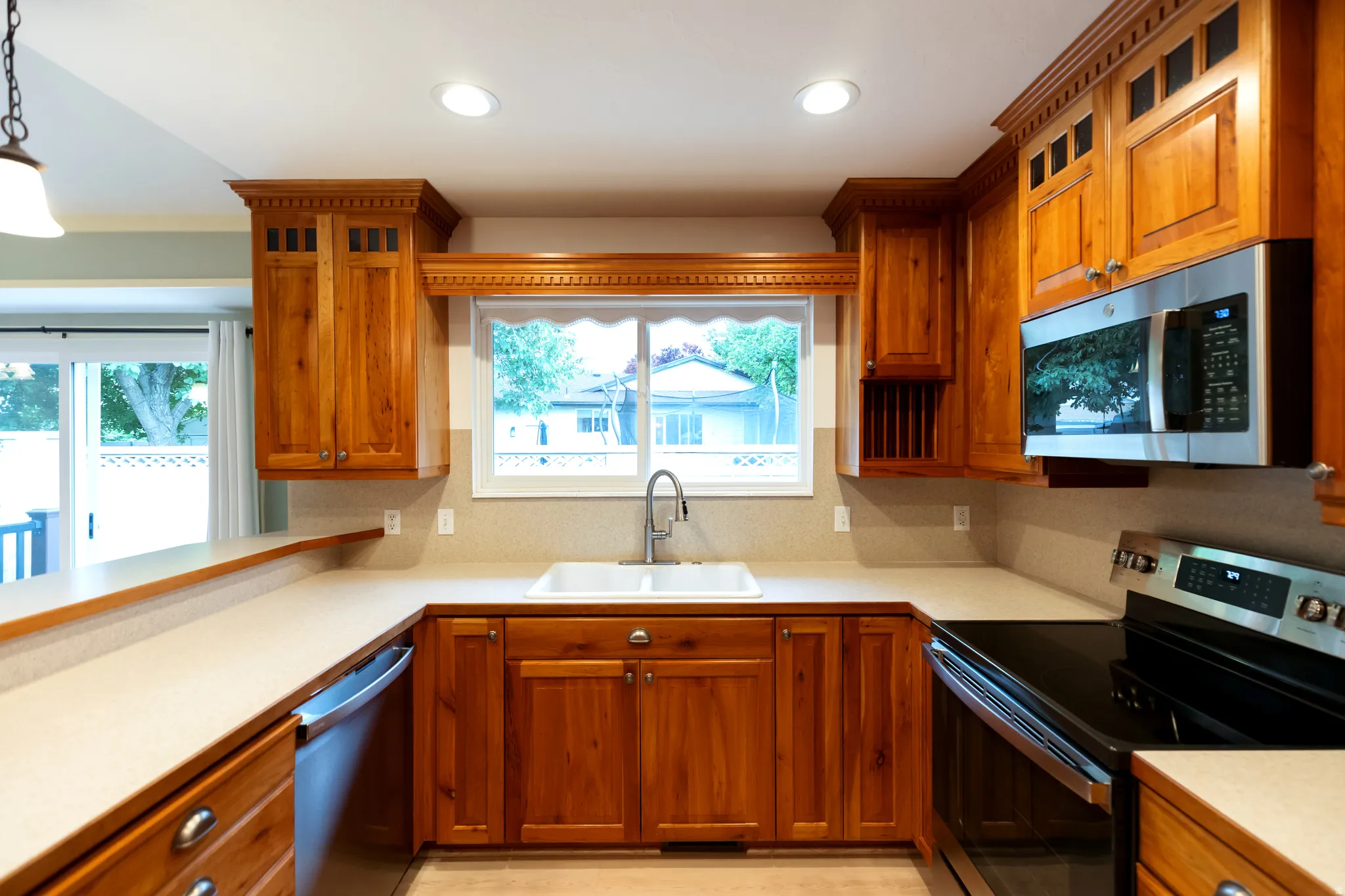 U-shaped kitchen featuring wood cabinetry, recessed lighting, stainless steel appliances, a double basin sink, and a sliding glass door