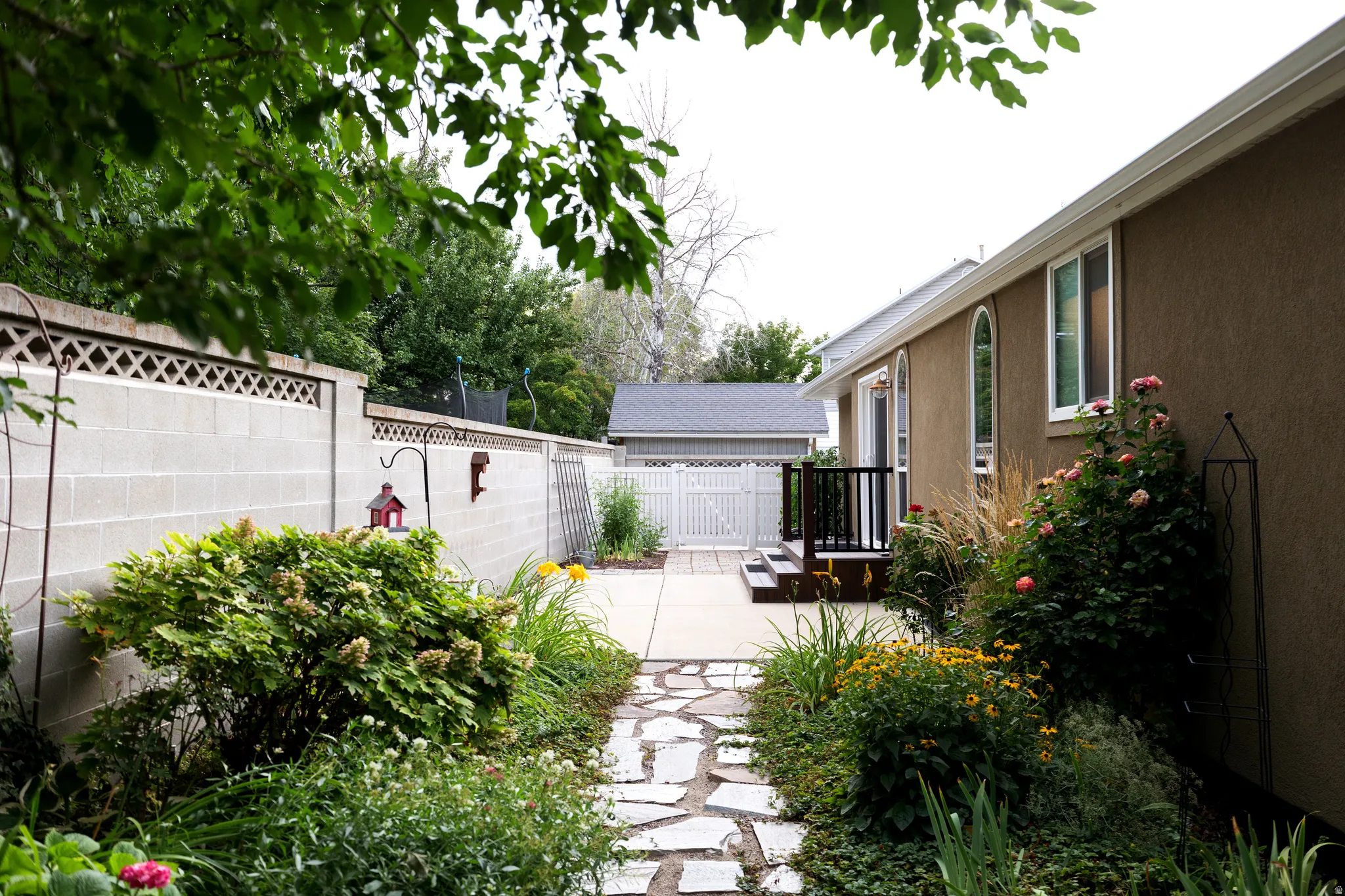 Landscaped garden path with flagstone pavers, mature plantings, and a block fence with decorative lattice top