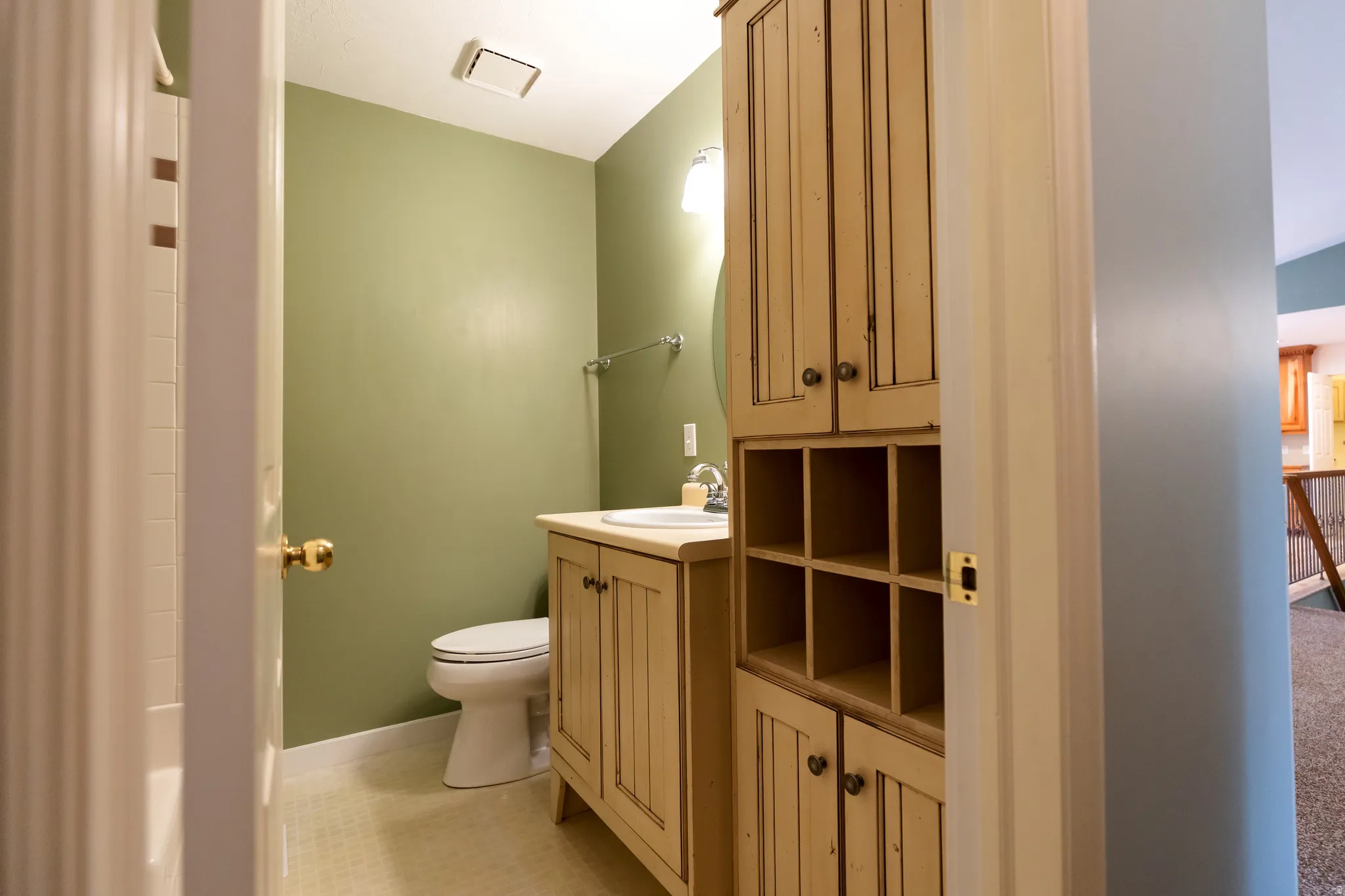 Bathroom featuring a wood-finish vanity with an integrated sink, coordinating wood-finish storage cabinetry with open shelving, a wall-mounted towel bar, and light-toned floor tiling