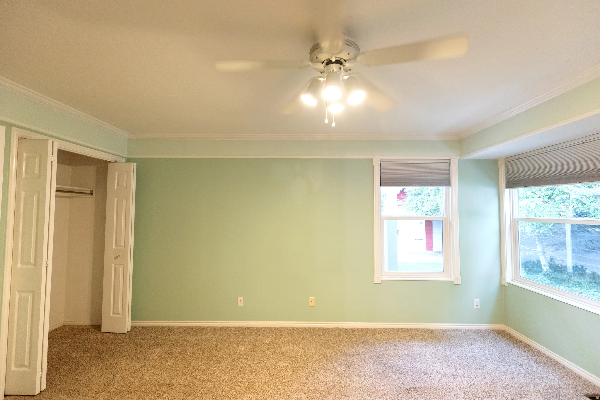 Spacious room featuring light green walls, a neutral carpeted floor, and a white ceiling fan with integrated lighting