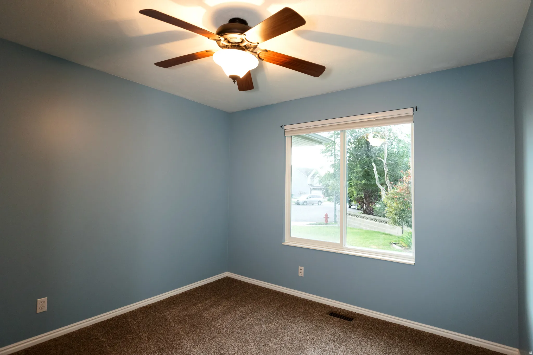Room featuring a ceiling fan with integrated lighting, a large window, light blue wall paint, and brown carpet flooring