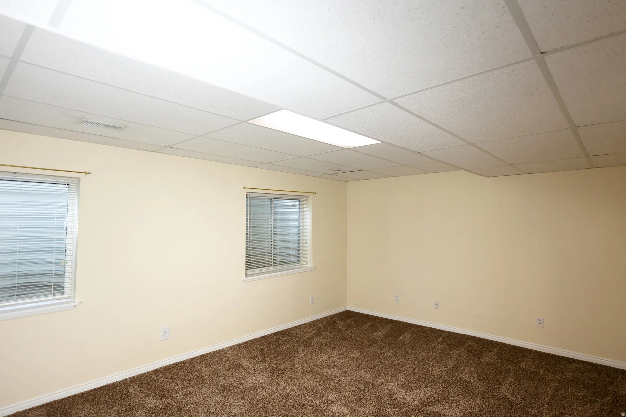 Spacious interior with neutral-toned walls, brown carpet flooring, and a white drop ceiling with recessed lighting