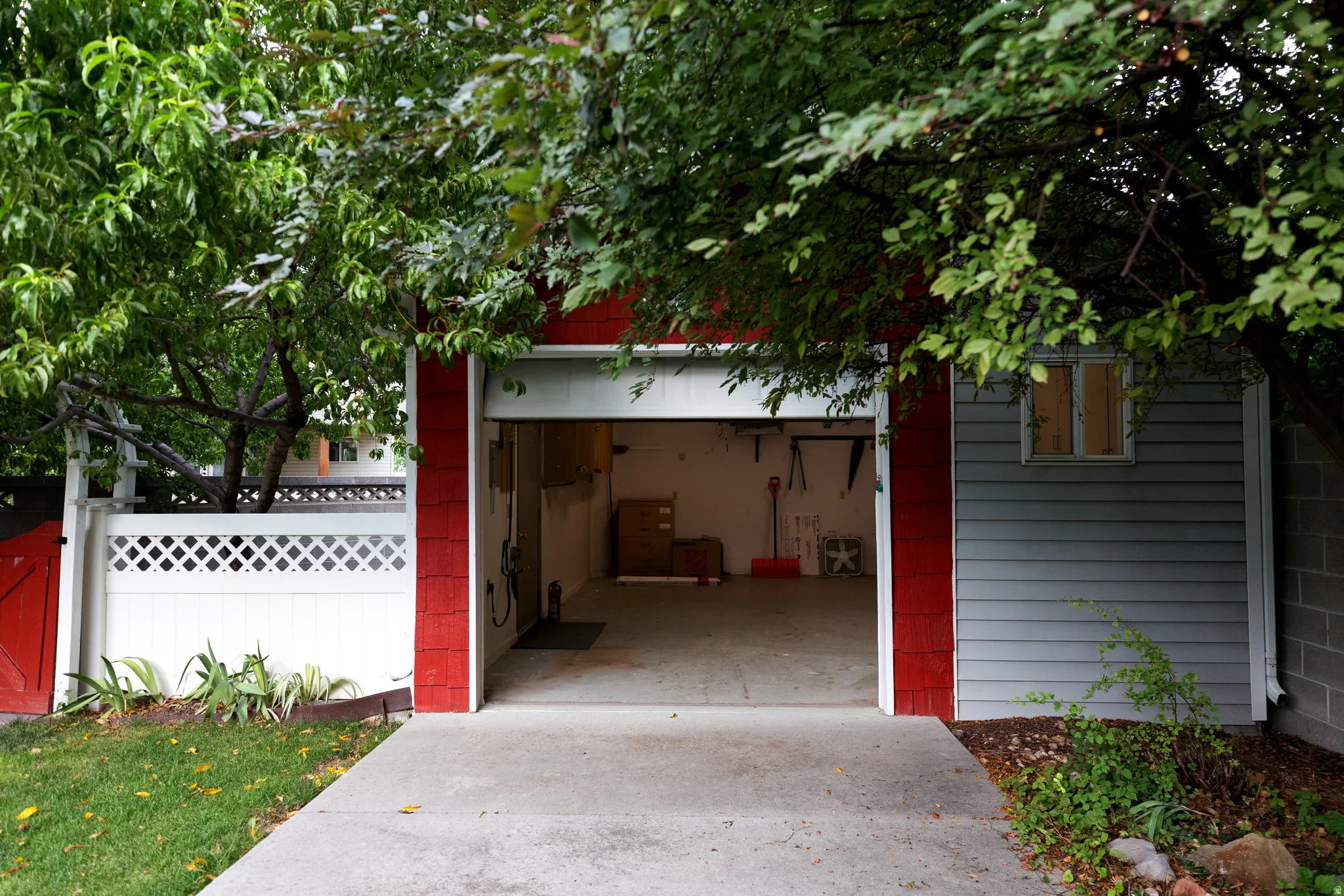 Attached garage with a concrete driveway, red and gray siding, and a white lattice fence