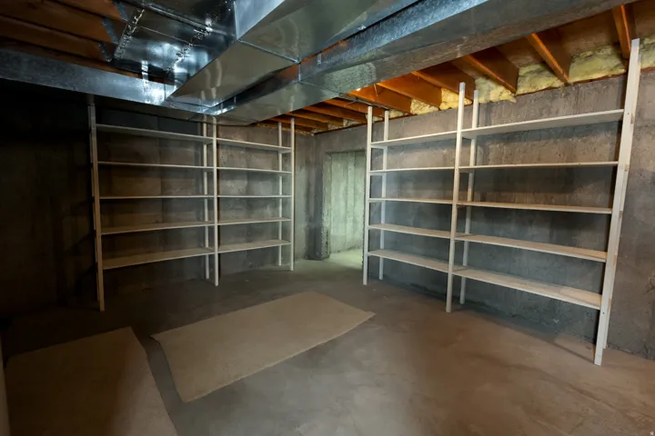 Unfinished basement featuring concrete flooring, exposed joists, and extensive built-in shelving units