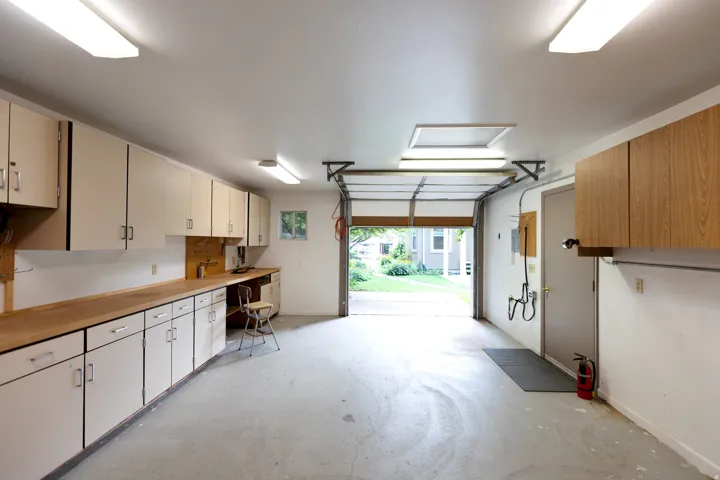Spacious garage featuring extensive built-in cabinetry, a wood-finish countertop workspace, and overhead fluorescent lighting