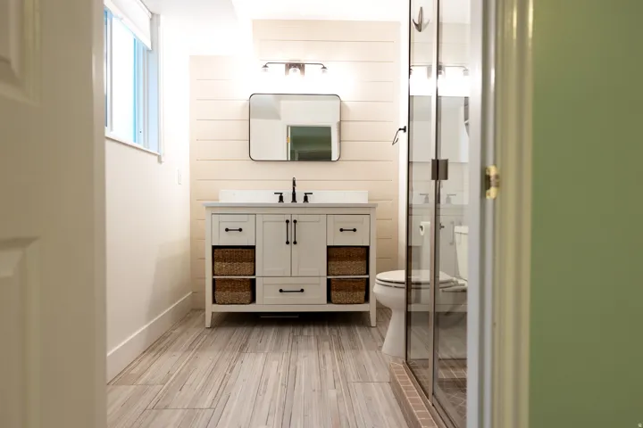 Modern bathroom featuring a white vanity with black hardware, plank-style wall paneling, and wood-finish tile flooring