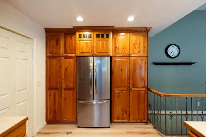 Custom wood-finish cabinetry with crown molding and integrated lighting, surrounding a stainless steel refrigerator