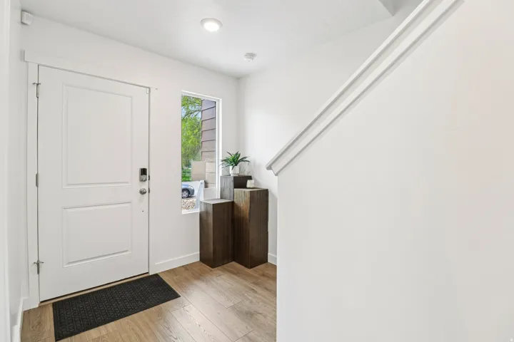 Entryway featuring a white paneled door, wood-finish flooring, a contemporary window, recessed lighting, and a white staircase with a prominent handrail