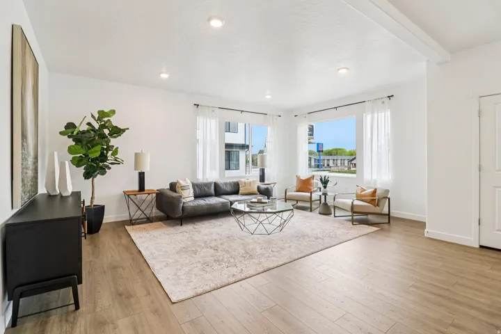Spacious living area featuring light wood-finish flooring, recessed lighting, and large windows with sheer privacy treatments