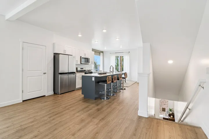 Open-concept kitchen featuring an island with seating, stainless steel appliances, white cabinetry, and wood-finish flooring