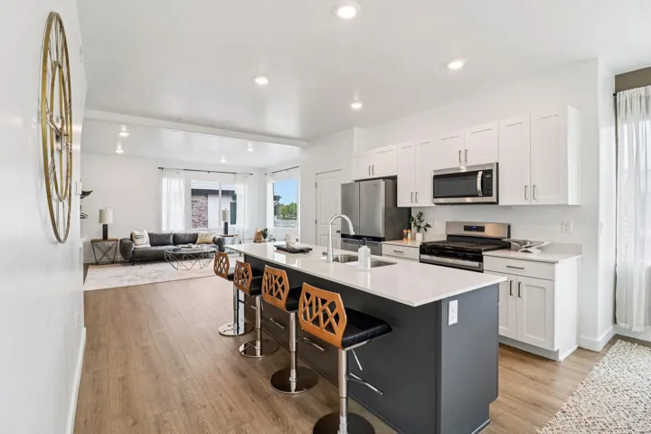 Modern kitchen featuring a large center island with seating, white shaker cabinetry, stainless steel appliances, and a gas range