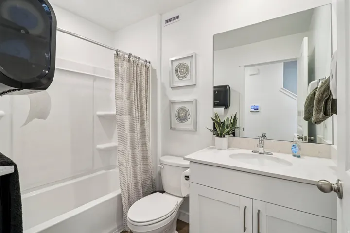 Full bathroom featuring a single vanity with a white countertop and undermount sink, a large wall-mounted mirror, a white toilet, and a white tub/shower combination with built-in shelving
