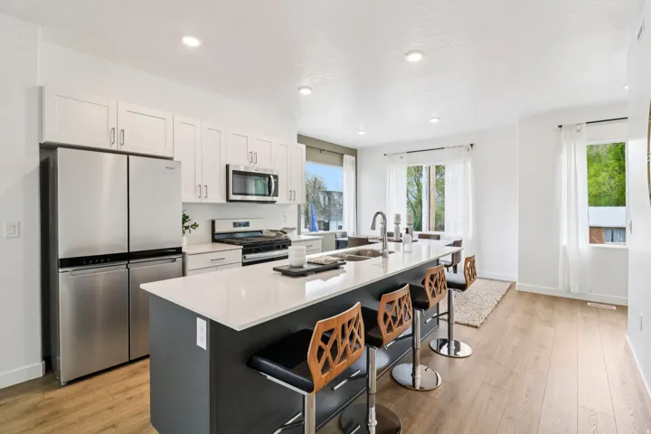 Modern kitchen featuring a large central island with seating, a stainless steel appliance suite, white shaker cabinetry, and wood-finish flooring