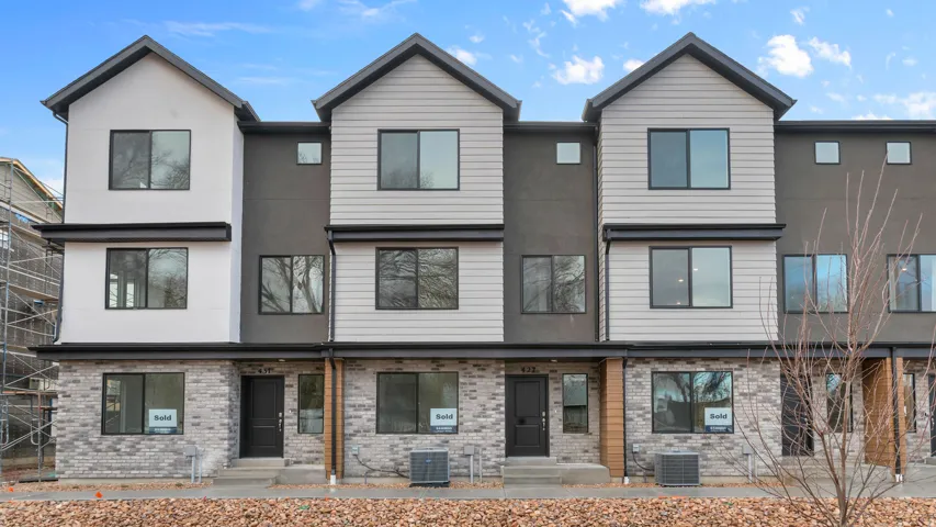 Modern multi-level townhome featuring a mix of light brick, vertical siding, and smooth stucco facade