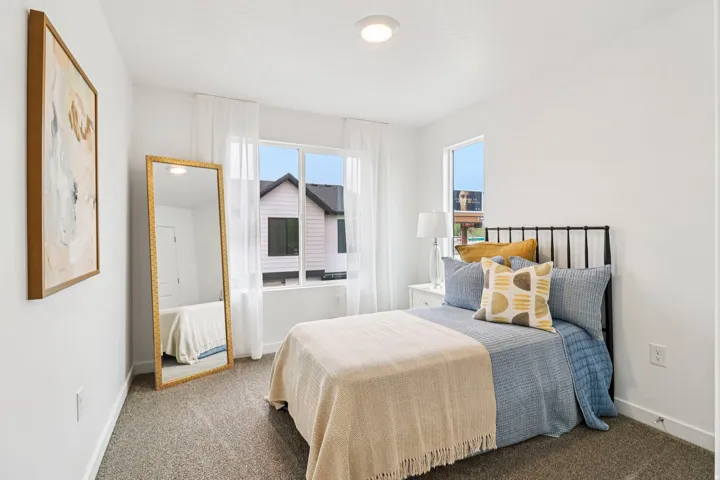 Bright bedroom featuring a large window with white sheer curtains, a second window, and neutral-toned carpeting